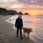 Woman walking golden retriever dog on beach at sunset